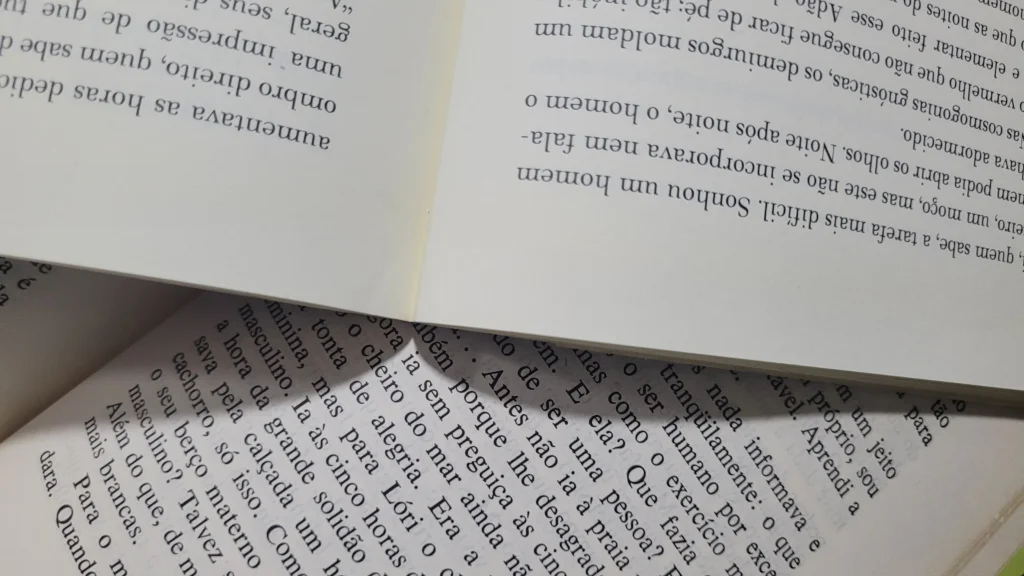 Vista aproximada de três páginas de livro sobrepostas em diferentes ângulos, exibindo texto impresso em língua portuguesa sobre papel de tom creme